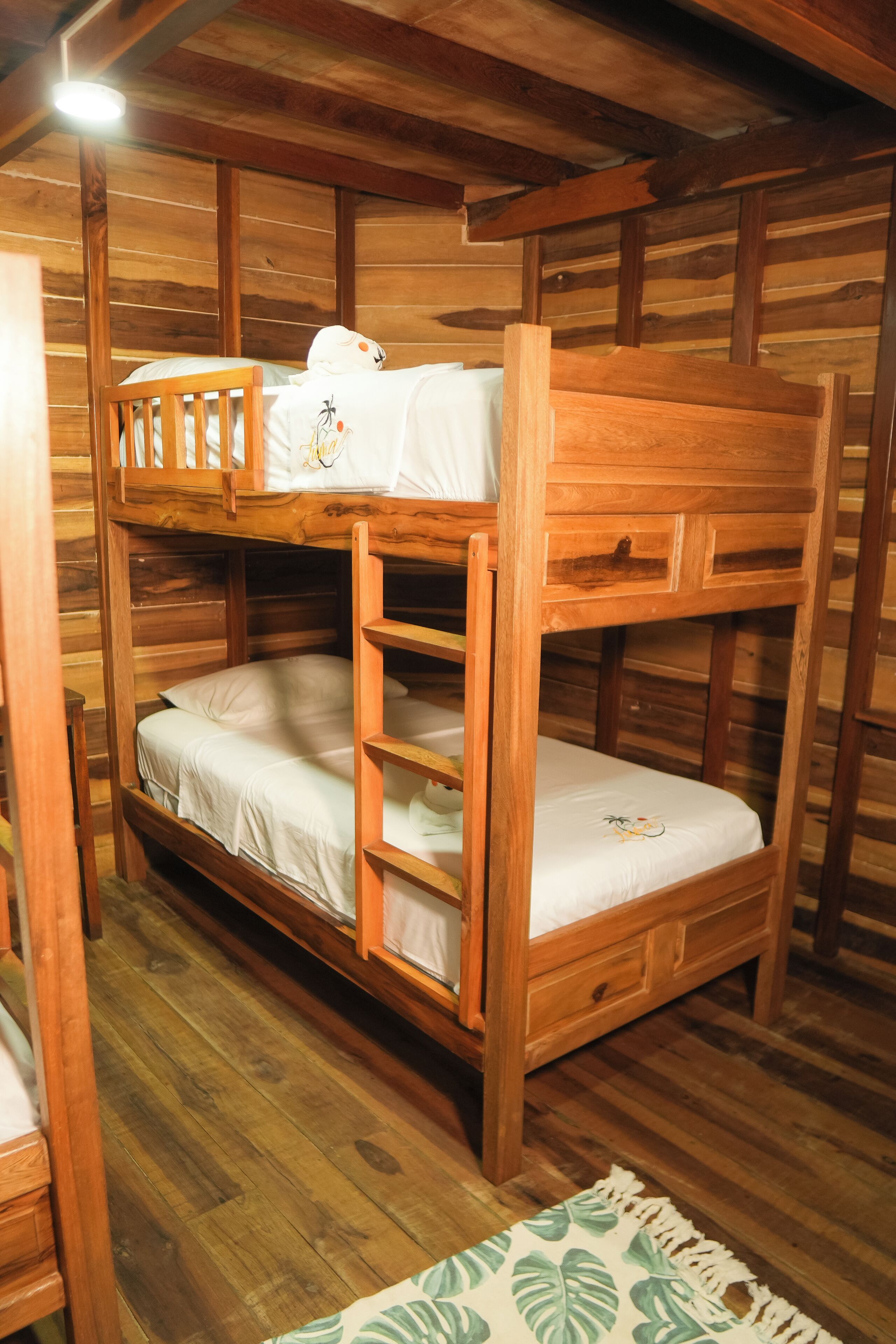 Habitación con literas, paredes y suelos de madera, una mesita de noche pequeña y una alfombra estampada.