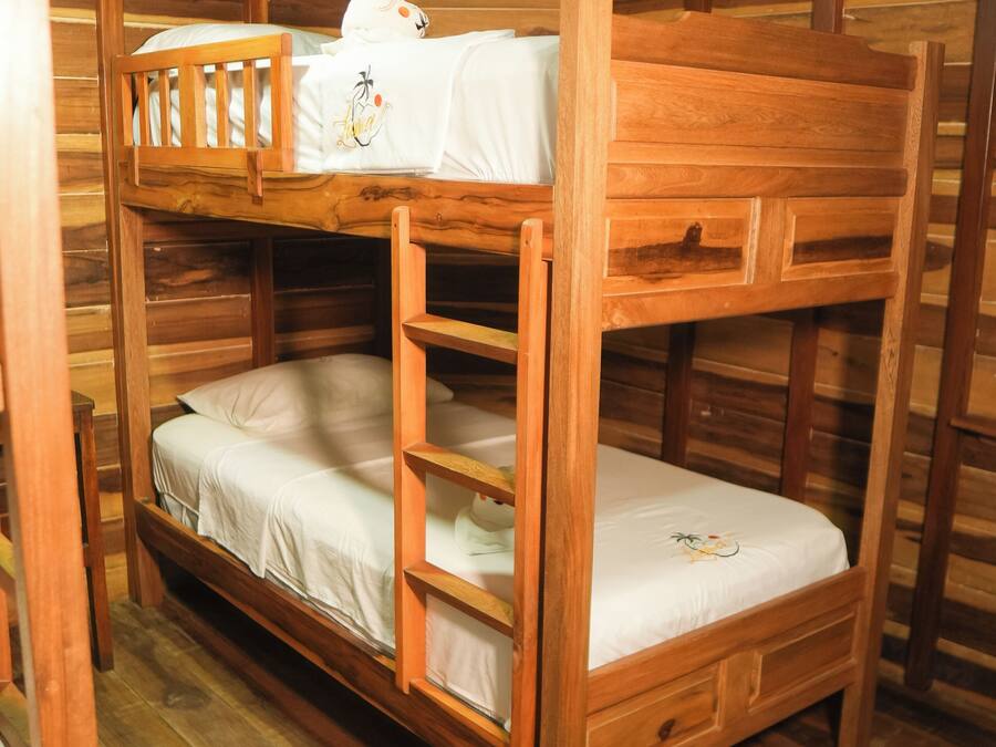Habitación con literas, paredes y suelos de madera, una mesita de noche pequeña y una alfombra estampada.