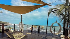 A deck with wicker furniture, a hanging chair, and a view of the ocean. - Luma at the beach (Santa Marta)