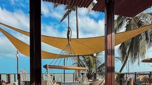 A wooden deck with a hammock, wicker furniture, and a view of the ocean and palm trees. - Luma at the beach (Santa Marta)