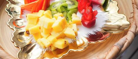 Una persona sosteniendo una cesta de mimbre con un borde dorado que contiene sandía cortada, kiwi, mango y fresas.