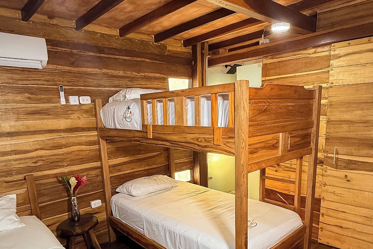 A rustic wooden cabin with bunk beds, a small table with a vase, and a wall-mounted air conditioner.