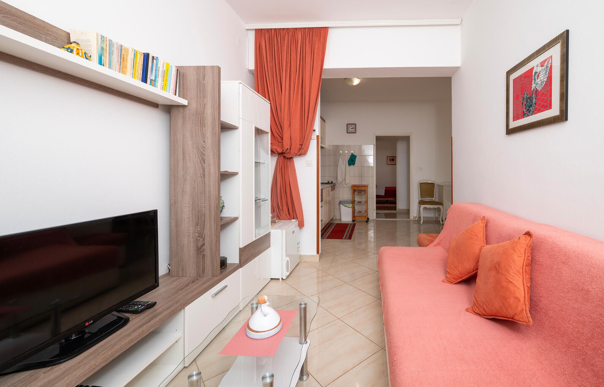 A living room with a flat-screen TV, a pink sofa, and a bookshelf with books and a backpack.