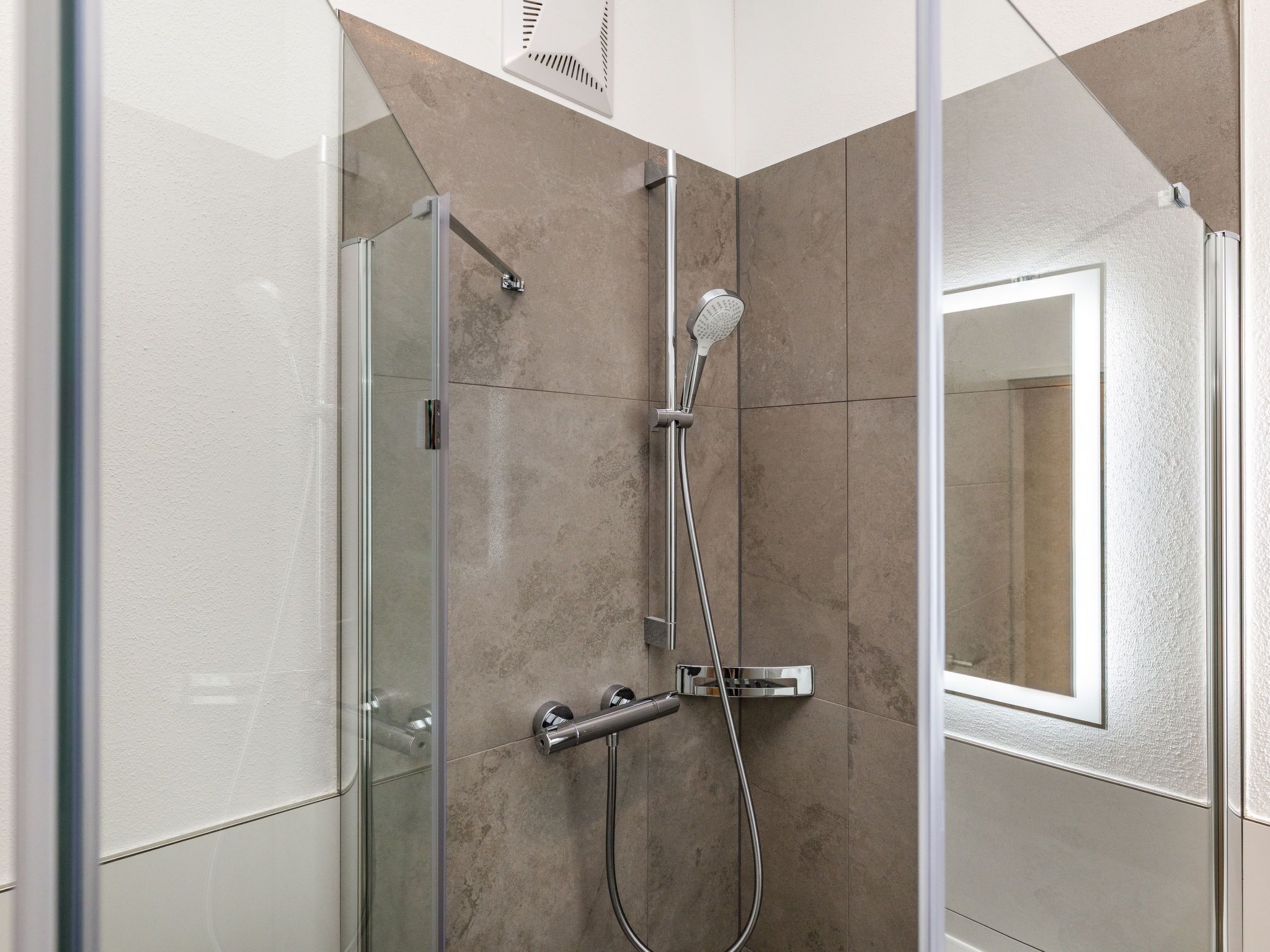 Eine moderne Dusche mit Glasabtrennung, einer Handbrause und einer fest installierten Bedienkonsole.
