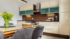 Eine moderne Küche mit Holzschränken, einem Edelstahlkochfeld und einem Essbereich mit einem Glastisch und Stühlen.
