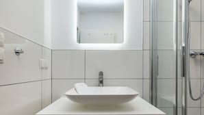 Une salle de bain moderne avec un lavabo blanc, un miroir et une douche.