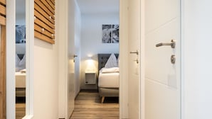 Un couloir étroit mène à une chambre à coucher qui contient un lit, une table de chevet et une œuvre d’art accrochée au mur.