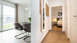 Un intérieur moderne comprenant un coin repas, un couloir menant à une chambre et une vue dégagée sur l’extérieur grâce à une grande fenêtre.