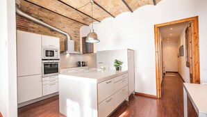 A modern kitchen with white cabinetry, a central island, and a brick ceiling.