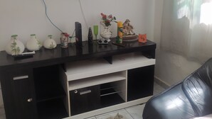 Un salon doté d’un téléviseur à écran plat fixé au mur, d’un meuble de rangement noir contenant divers objets, d’un tapis moelleux et d’un canapé en cuir.