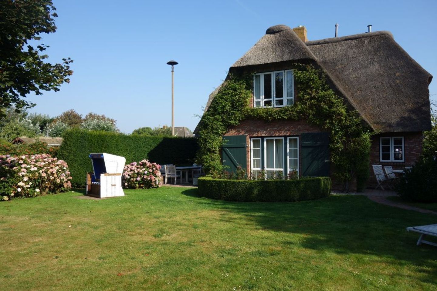 A thatched-roof house with a well-maintained garden, a street lamp, and a bench.