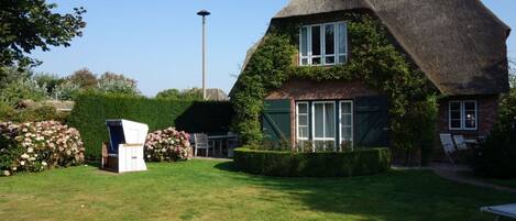 A thatched-roof house with a well-maintained garden, a street lamp, and a bench.