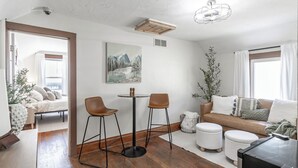 Un soggiorno moderno con pavimento in legno, un tavolino rotondo con due sedie, un divano, un tavolino da caffè e un quadro appeso al muro.