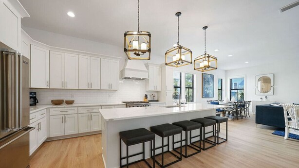 A modern kitchen with white cabinetry, a central island with bar stools, and pendant lighting. - Get Busy Livin! on 30A (Santa Rosa Beach)