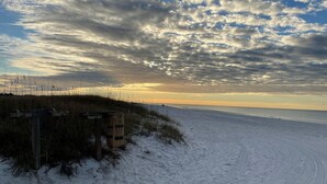 A beach with a wooden fence and signs, a sandy path leading to the water, and a cloudy sky. - Get Busy Livin! on 30A (Santa Rosa Beach)