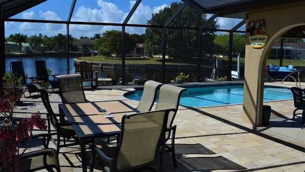 Un espacio al aire libre techado con piscina, sillas de descanso y vista a un lago.