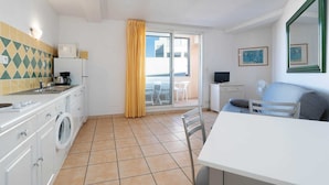 A compact kitchen with a washing machine, a coffee maker, and a small dining area with a table and chairs. - Comfort with Sunlit Balcony (Agde)