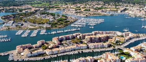 Vista aérea de una ciudad costera con un puerto deportivo lleno de barcos, rodeada de edificios residenciales y un puente que conecta diferentes zonas.