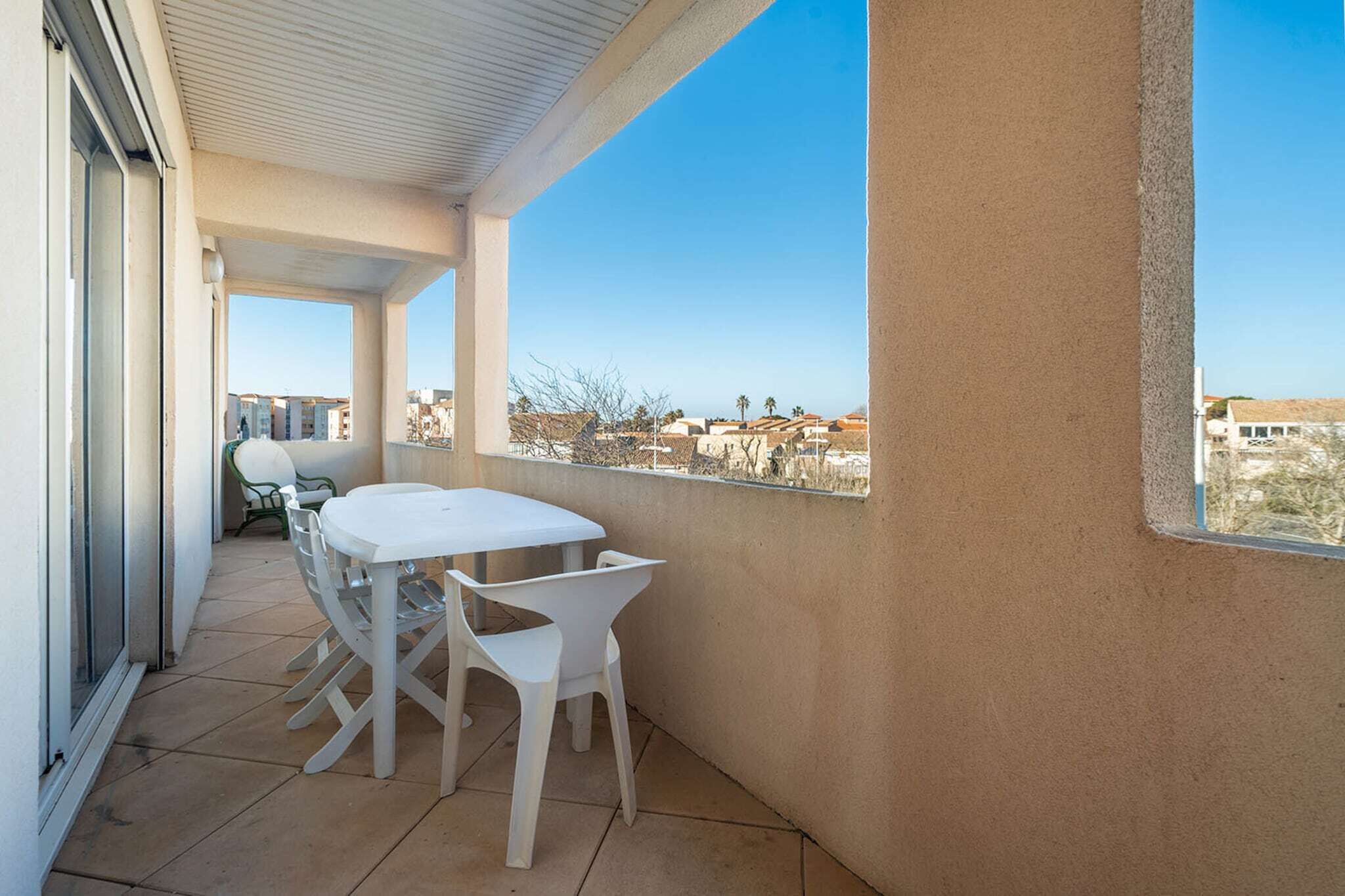 Ein Balkon mit einem weißen Tisch und Stühlen, Blick auf Gebäude in der Ferne und einem klaren Himmel.