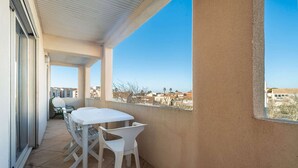 A balcony with a white table and chairs, a view of buildings in the distance, and a clear sky. - Comfort with Sunlit Balcony (Agde)