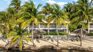 Ein Resort mit Palmen, Reetdachschirmen und einem Gebäude mit Balkonen.