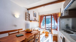 A cozy kitchen with wooden furniture, a dining table with fruit, and a large window with curtains. - Apartment in Morillon near Ski Slopes (Morillon)