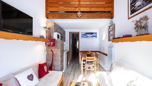 A cozy room with a sofa, a wooden table, a TV, and a kitchen area. - Apartment in Morillon near Ski Slopes (Morillon)