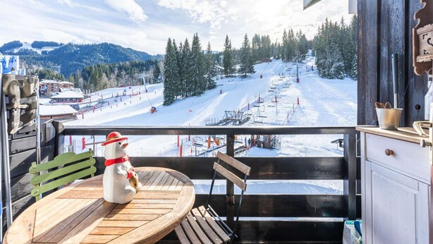 A balcony with a view of a snowy ski slope, a wooden table, and a snowman decoration. - Apartment in Morillon near Ski Slopes (Morillon)