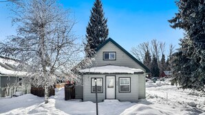 Een klein huis met een besneeuwde voortuin en een metalen hek.