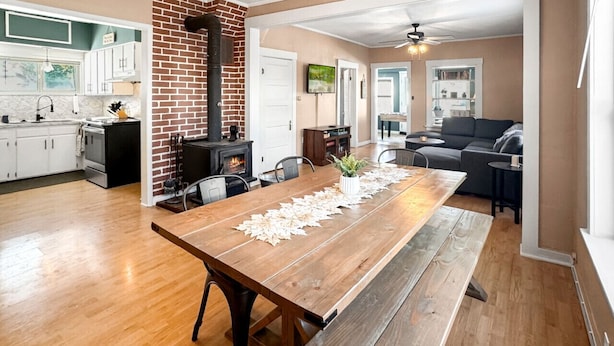 Een ruime woonkamer met een lange houten eettafel, een open haard en een moderne keuken op de achtergrond.