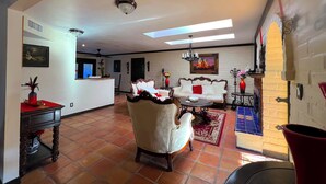 A spacious living area with a sofa, a coffee table, and a fireplace. There is a dining area with a table and chairs, and a kitchen in the background.