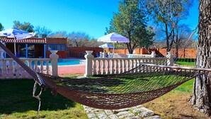 A hammock tied between two trees in a landscaped area with a pool and outdoor seating.