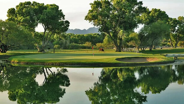 A serene golf course with a pond reflecting trees and a distant mountain range.