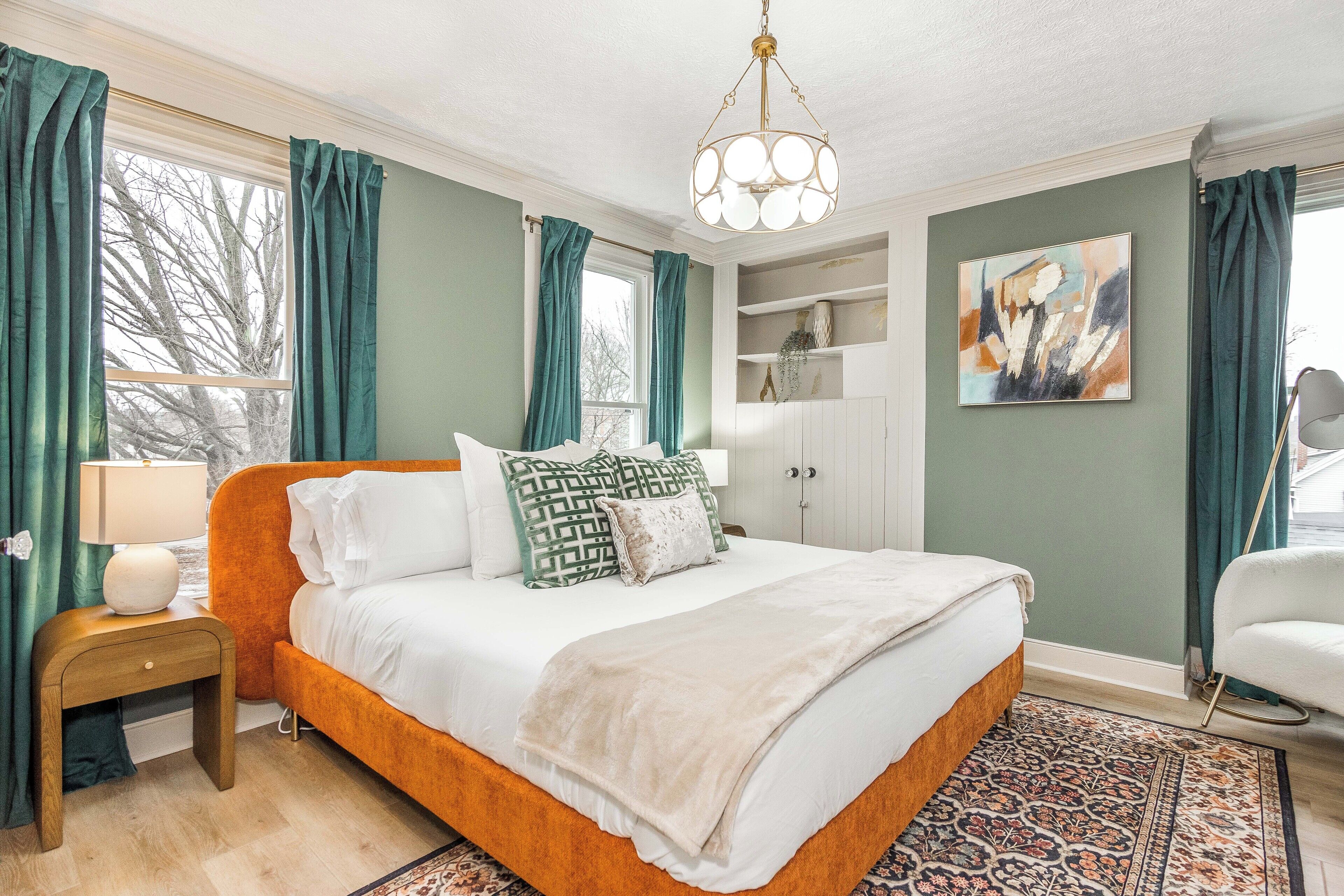 Um quarto com uma cama grande, uma mesa de cabeceira, um penteado, uma cadeira e uma janela com cortinas.