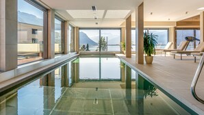 A modern indoor swimming pool with clear views of mountains and a lake.