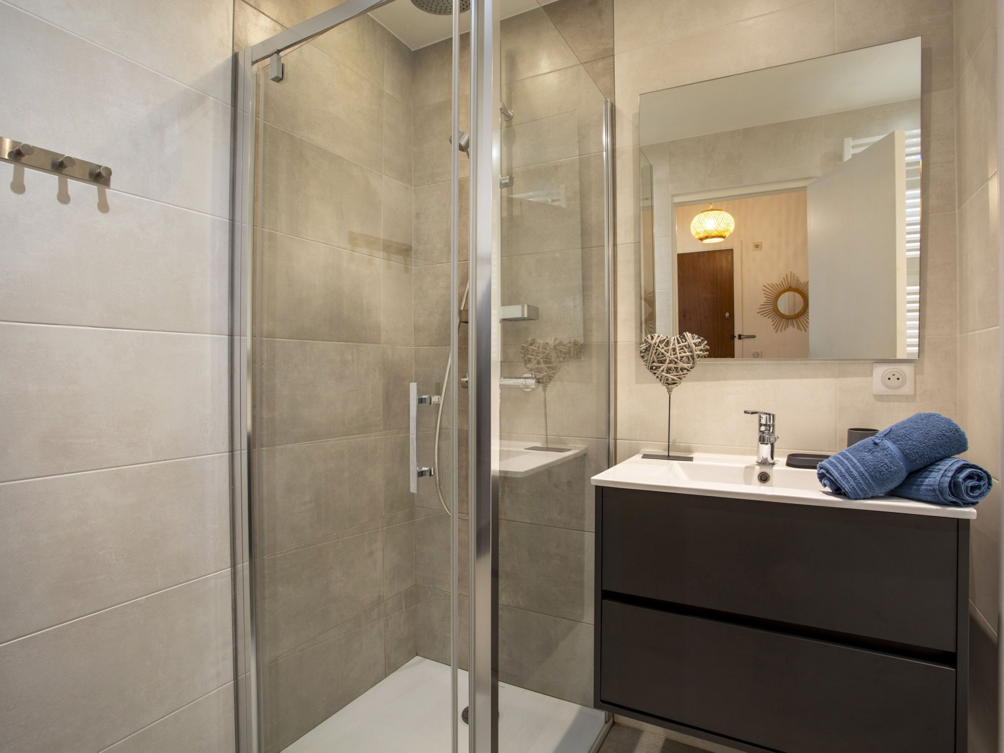A modern bathroom with a glass shower enclosure, a white sink with a dark cabinet, and a mirror above the sink.