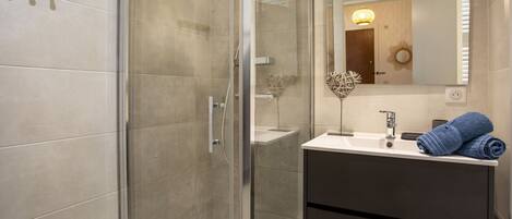 A modern bathroom with a glass shower enclosure, a white sink with a dark cabinet, and a mirror above the sink.