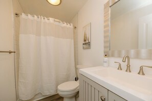 Bathroom features a shower curtain, toilet, and sink with modern faucet.
