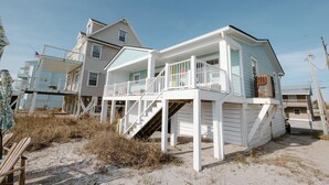A beachfront house with a balcony, a staircase leading to the main floor, and a small porch area. - Oceanfront Cottage with Private Beach Area! (Carolina Beach)