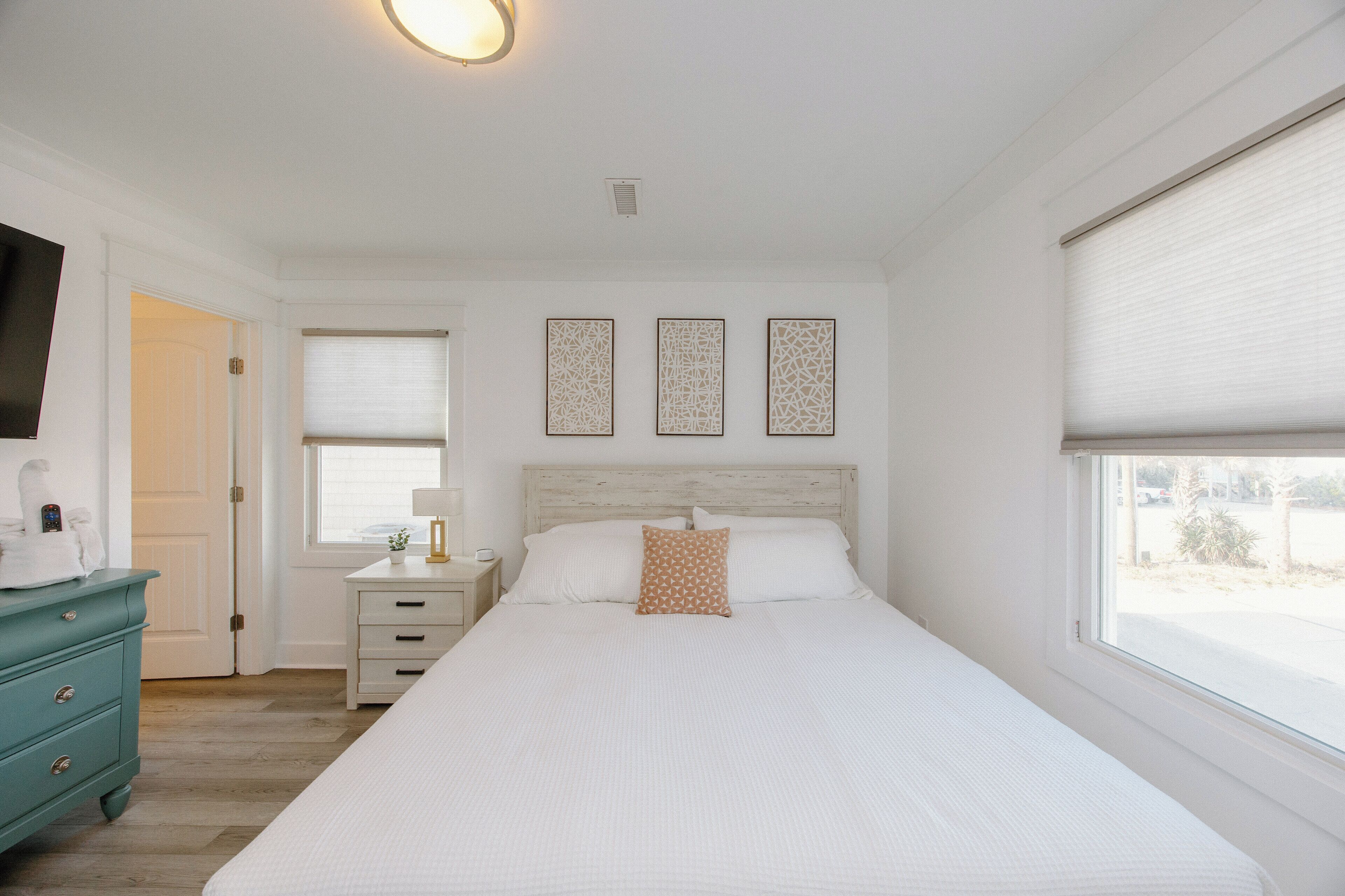 A bedroom with a large bed, a nightstand, a dresser, and a window with blinds.