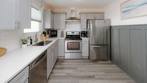 A modern kitchen with stainless steel appliances, white cabinetry, and a wooden countertop. - Oceanfront Cottage with Private Beach Area! (Carolina Beach)