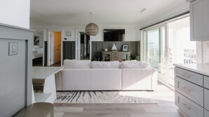 A modern living room with a white sofa, a dining area, and a kitchen. - Oceanfront Cottage with Private Beach Area! (Carolina Beach)