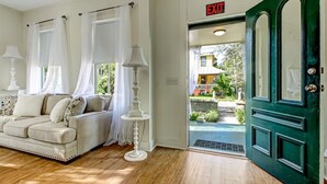 A room with a beige sofa, white curtains, a white lamp, and a green door with an exit sign.