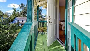 Une véranda avec une balustrade verte, une porte blanche et une vue sur une maison au loin.