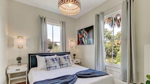 Une chambre à coucher avec un lit, des tables de chevet, une lampe, un tableau et une fenêtre avec des rideaux.