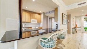 A modern kitchen with a black countertop, wooden cabinets, a microwave, and two wicker chairs.