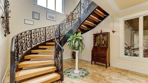 Una escalera de caracol con barandales de metal ornamentados y escalones de madera, que conduce a una zona de descanso con una planta en maceta y un armario de madera.