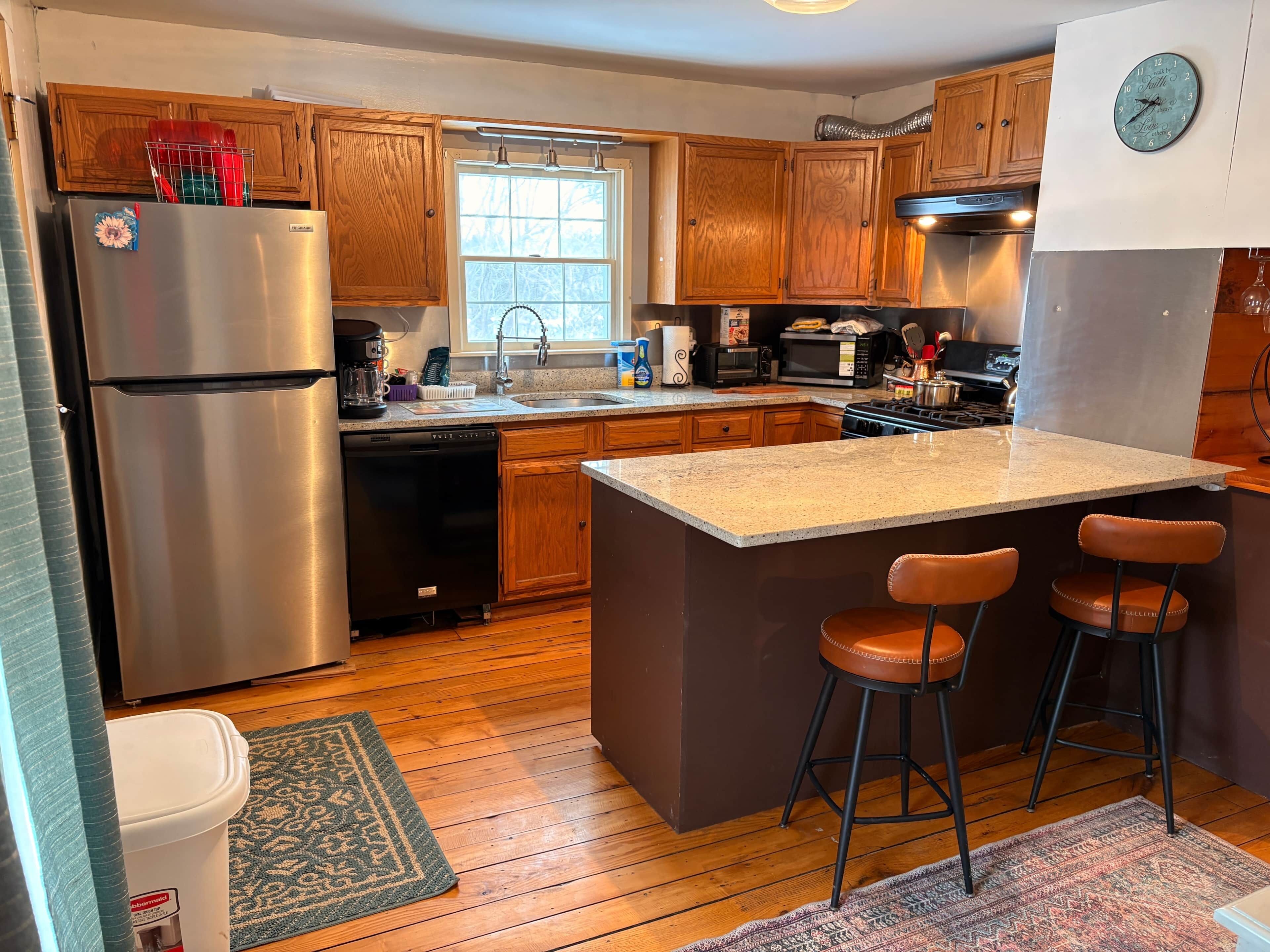 A kitchen with wooden cabinets, a stainless steel refrigerator, a dishwasher, a microwave, a stove, and a large island with bar stools.