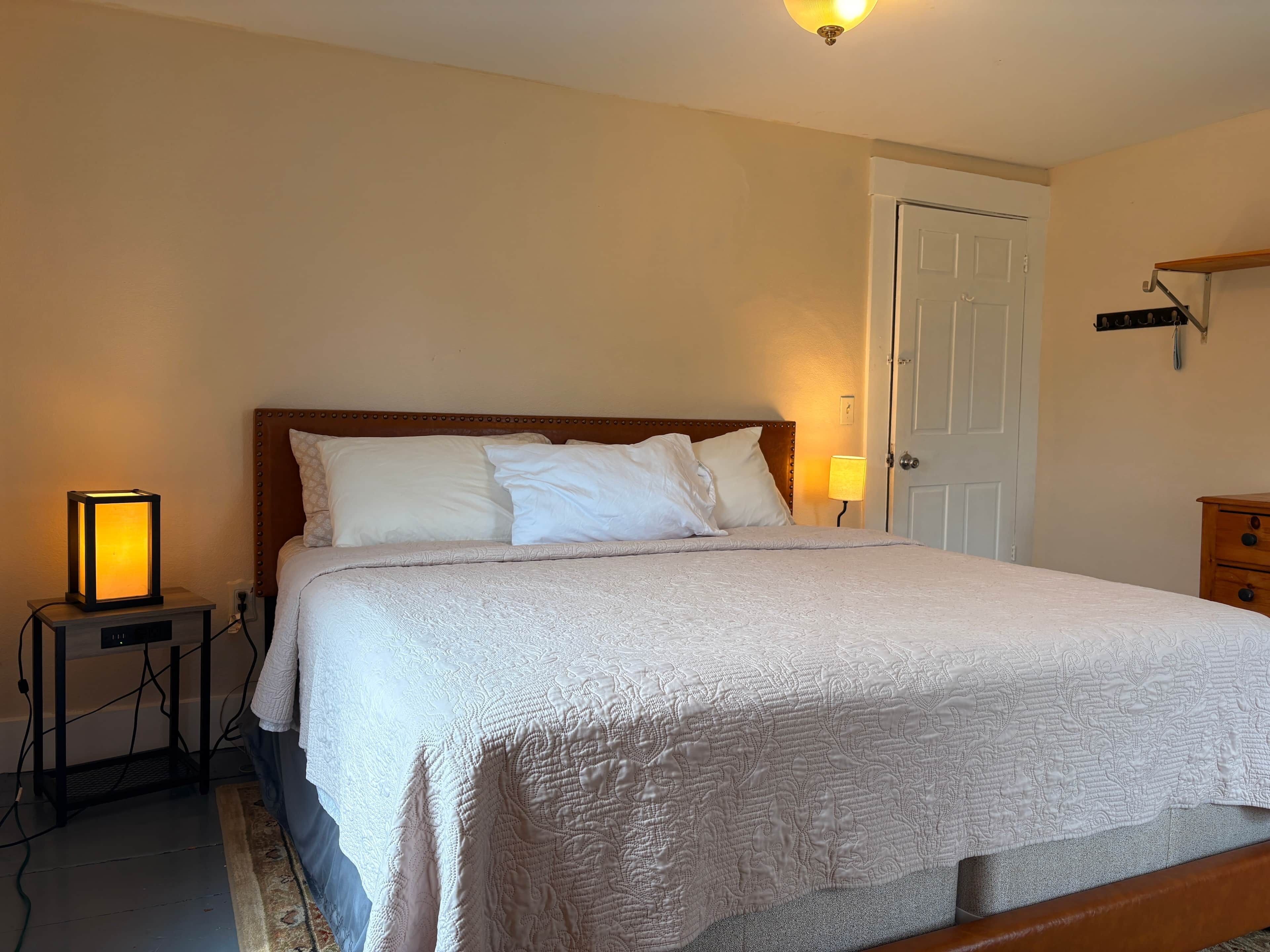 A neatly made bed with a patterned bedspread, a bedside lamp, and a nightstand with a lamp.
