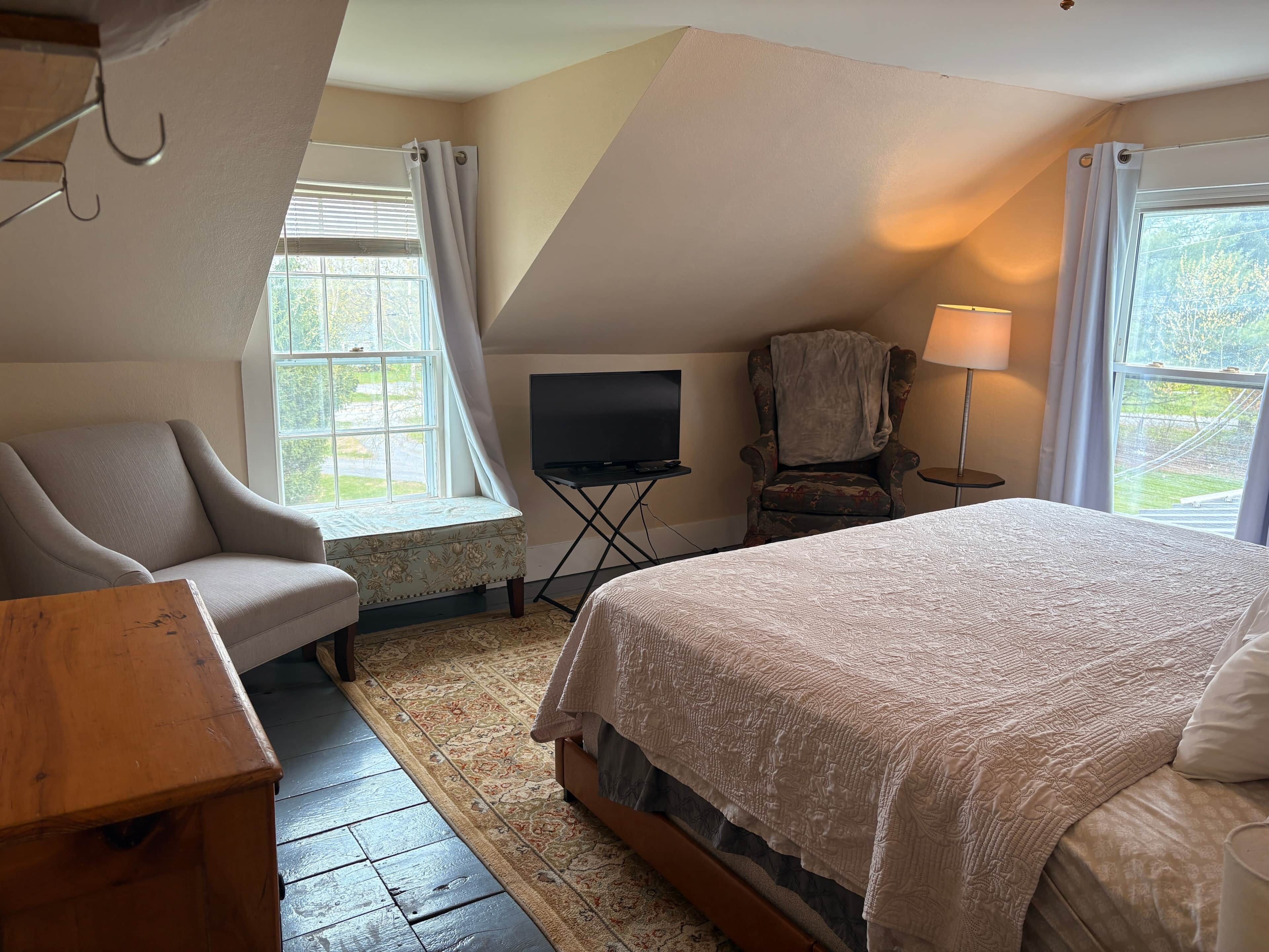 A bedroom with a bed, a chair, a television, and a lamp.